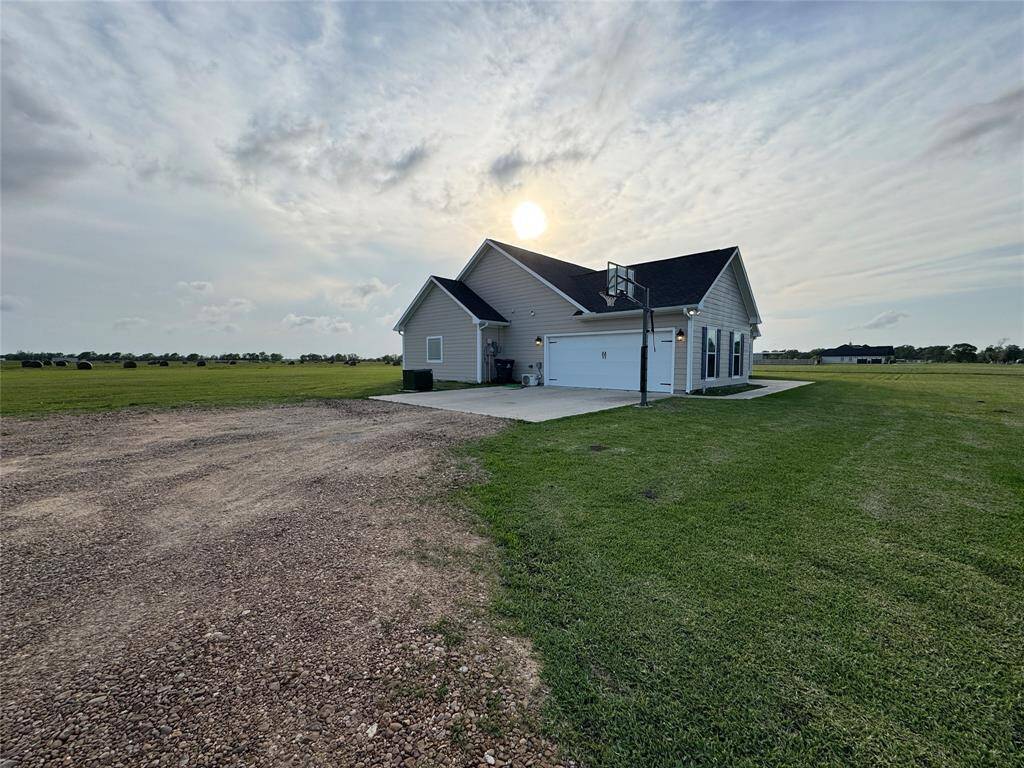 This house is a modern, single-story home with a large attached garage, set on a spacious plot of land with expansive green fields. The setting offers a serene, rural atmosphere with plenty of open space.