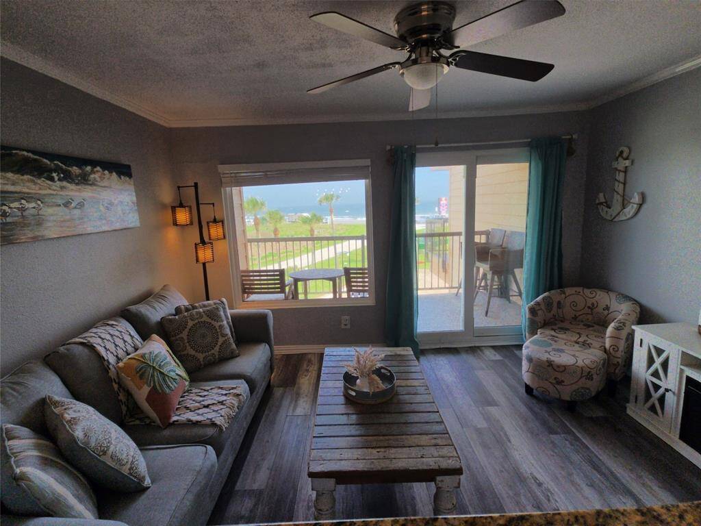 This cozy living room features a comfortable sofa, stylish armchair, and rustic coffee table. It offers a bright, open feel with large windows and sliding doors leading to a balcony with gorgeous Gulf views. The room is accented by a ceiling fan and coastal decor.