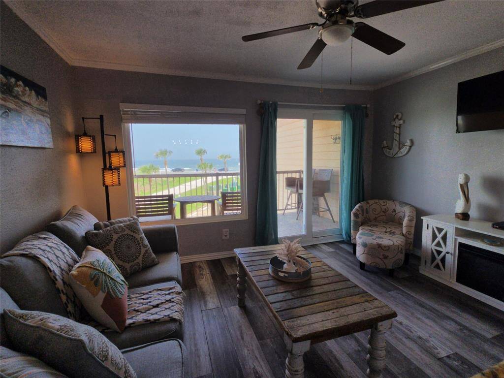 Cozy living room with a modern coastal vibe, featuring a comfy sofa, stylish accent chair, and a ceiling fan. The space opens to a balcony with ocean views, perfect for relaxation.