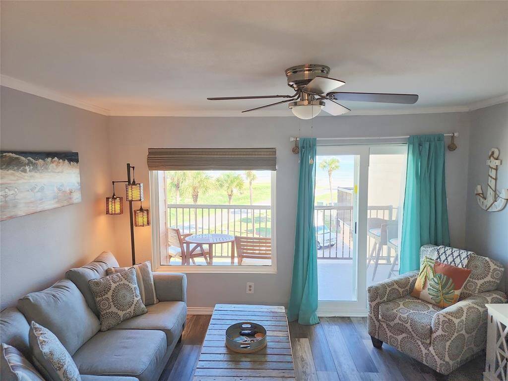 Bright and cozy living room with ocean views, featuring a ceiling fan, comfortable seating, and nautical decor. Sliding glass doors lead to a balcony, enhancing the open and airy feel.