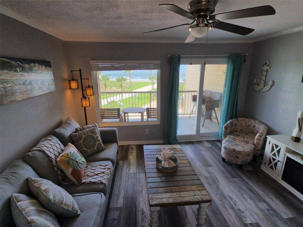 This photo showcases a modern kitchen with stainless steel appliances, granite countertops, and a stylish light fixture. The open layout includes a breakfast bar with stools, leading into a cozy living area with laminate wood flooring and tasteful decor.