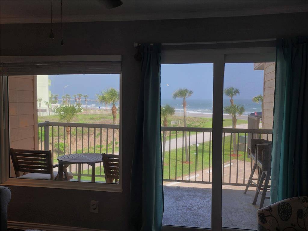 This photo showcases a living space with large windows and a sliding glass door leading to a balcony. The view features palm trees and the gulf creating a serene coastal atmosphere. The balcony includes a small table and chairs, perfect for enjoying the scenery.