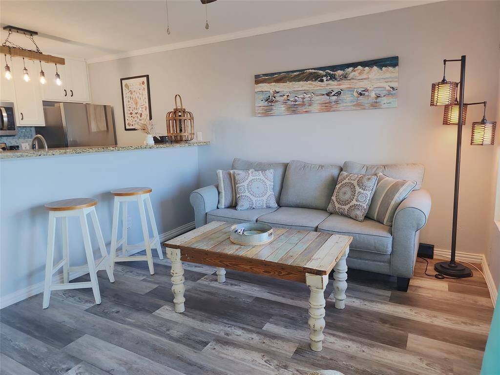 This photo showcases a modern, open-concept living space with a cozy kitchen area. The kitchen features stainless steel appliances, granite countertops, and a stylish light fixture. The room has hardwood floors, a ceiling fan, and is tastefully decorated, offering an inviting atmosphere perfect for relaxation and entertaining.