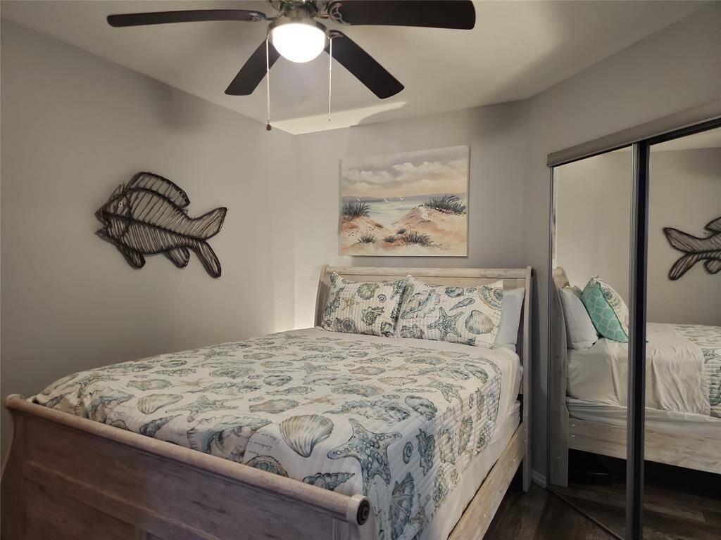 This cozy bedroom features a comfortable bed with beach-themed linens, a ceiling fan, a mirrored closet, and coastal decor, creating a relaxing, seaside ambiance.