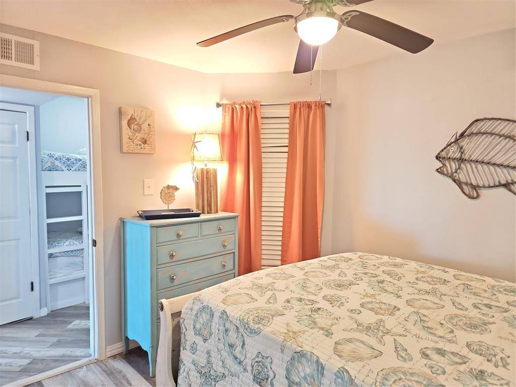 Cozy bedroom with a ceiling fan, mirrored closet doors, and direct access to a bathroom. Features a light, beach-themed decor with a patterned quilt and turquoise dresser.