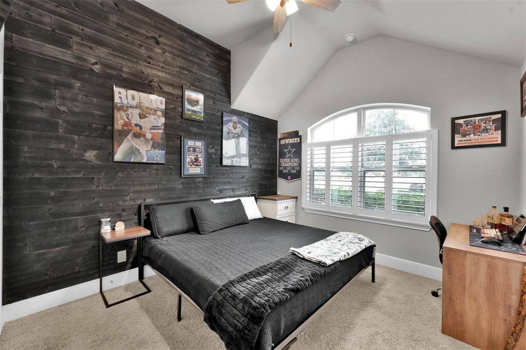 This bedroom features a custom shiplap feature wall, a vaulted ceiling with ceiling fan, and a large arched window with shutters for natural light.
