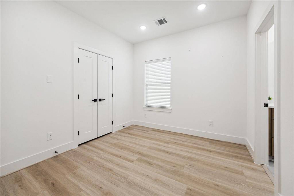 The spacious secondary bedroom features wood-look LVP flooring, recessed lighting, and a large window that fills the room with natural light