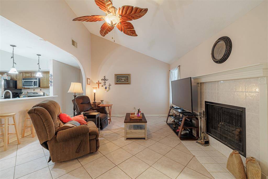 The spacious family room features soaring ceilings, tile floors, a cozy woodburning fireplace, and opens to the kitchen.