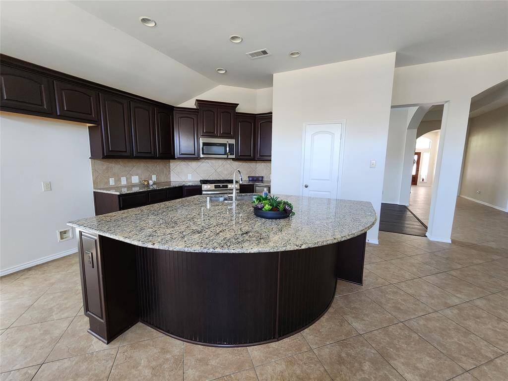 The gourmet kitchen is a chef’s dream, featuring a stunning circular granite island with seating for four, perfect for casual dining and entertaining.