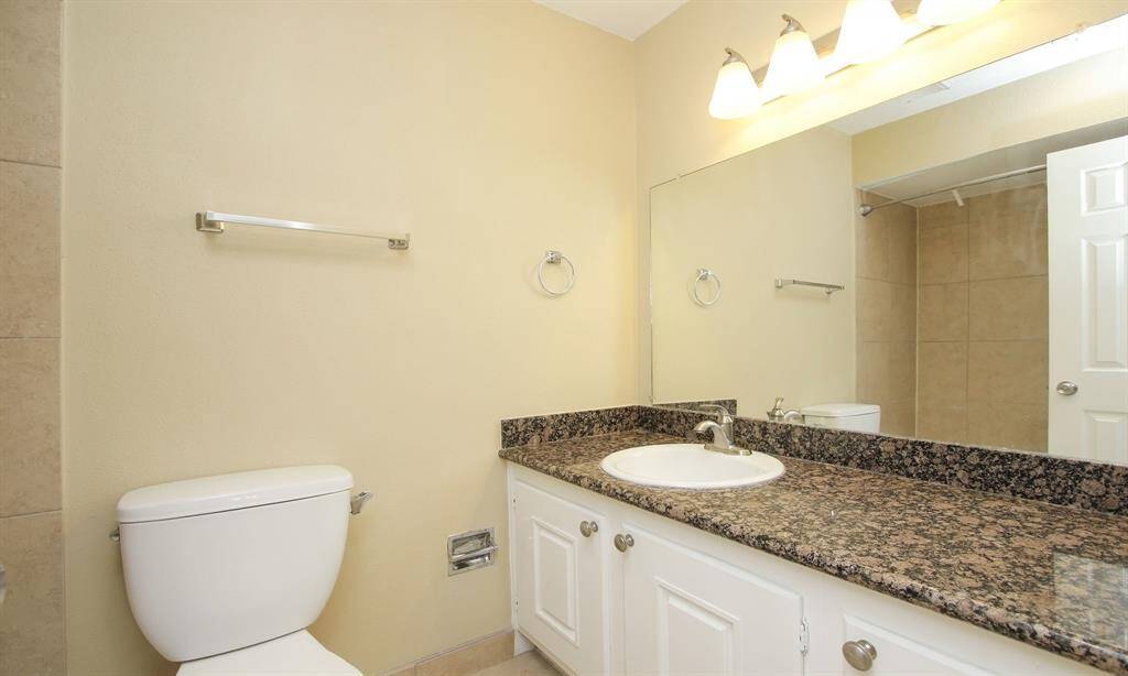 This is a well-maintained  master bathroom featuring a large vanity with granite countertop, under-mount sink, and ample cabinet space. It includes a toilet and a full-size shower/tub combo with tile surround. The space is well-lit with a strip of lights above the mirror.