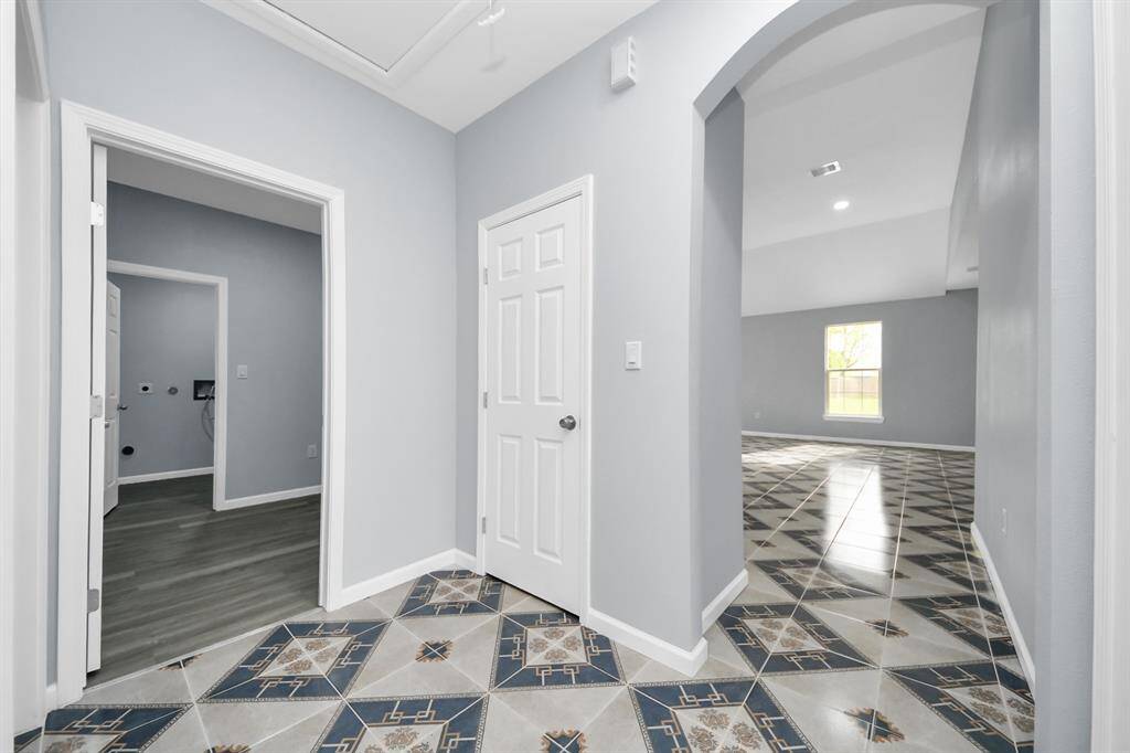 This photo showcases a bright entryway with decorative tiled flooring, leading to a spacious room with large windows. The walls are painted in a soft, neutral color, and there are multiple doorways, providing easy access to different areas of the home.
