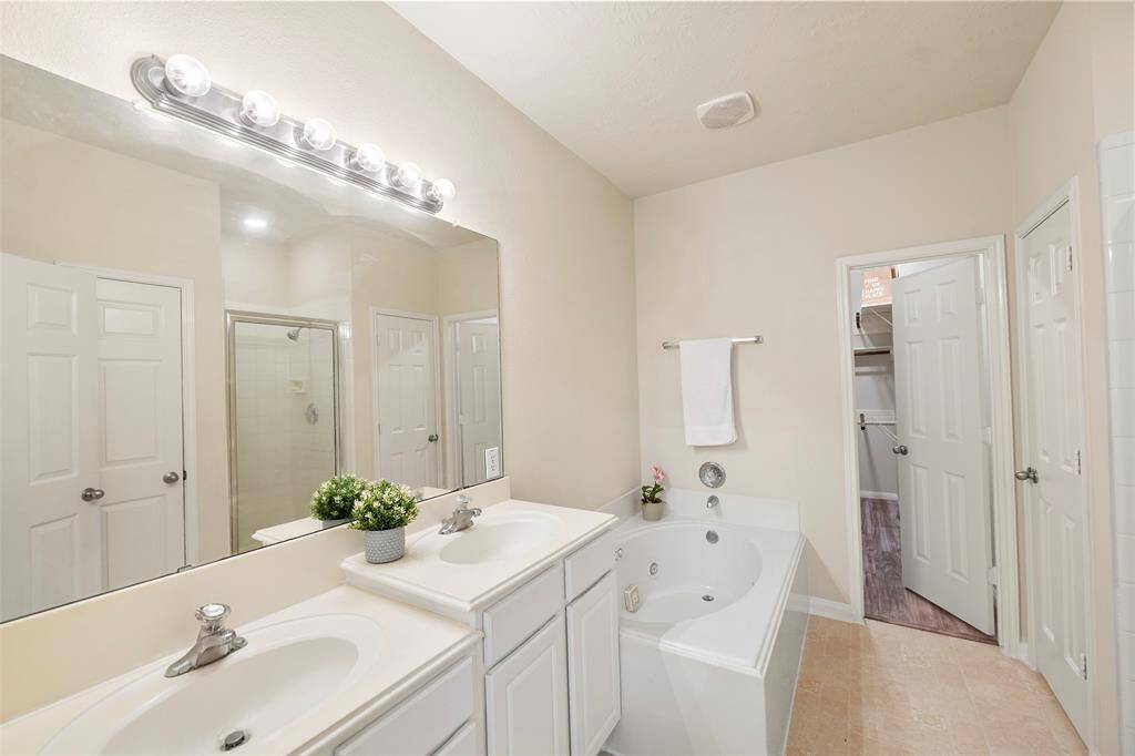 Primary bathroom with dual sinks, whirlpool tub, separate shower, and primary closet for all your things