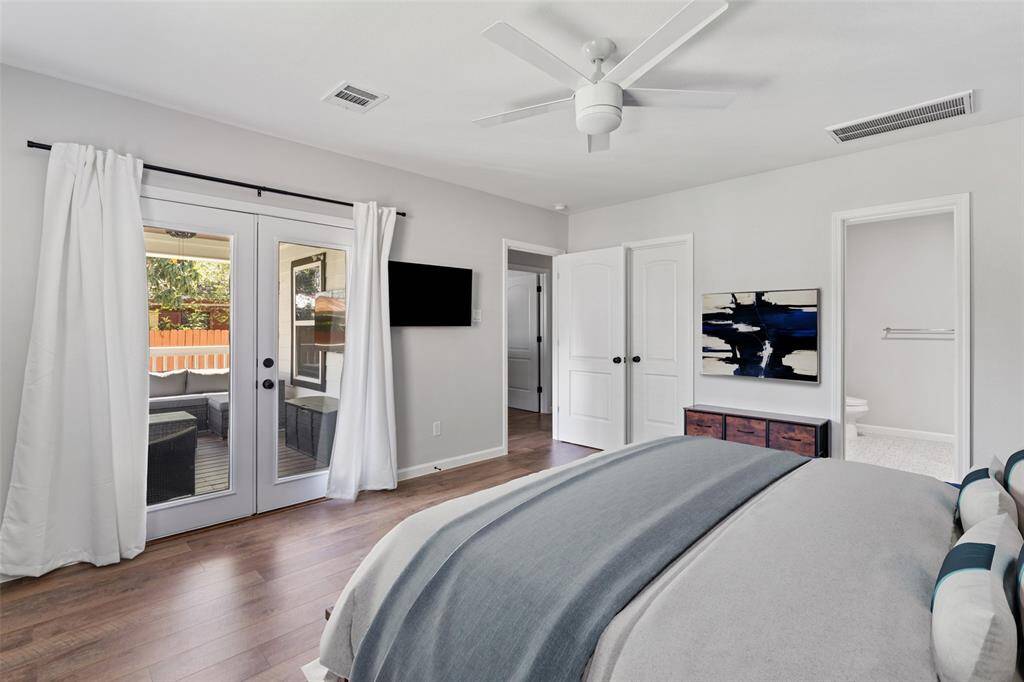 The primary suite’s refined simplicity is evident in its generous footprint, high ceilings, and seamless transition to the covered rear porch via French doors. Neutral gray walls and wide-plank flooring provide a serene backdrop for rustic-chic furnishings, while abundant natural light through multiple exposures creates a tranquil retreat.