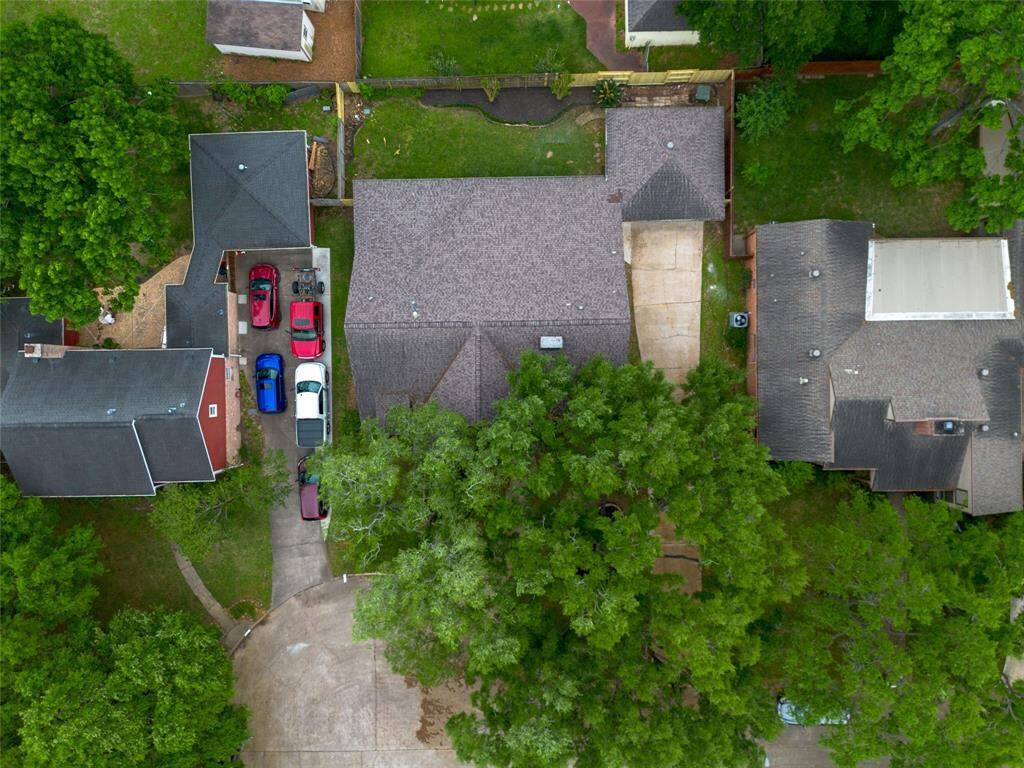 This aerial photo shows the front view of the home  surrounded by lush greenery. This house has a spacious driveway and is nestled among trees, offering privacy. The area is peaceful and well-maintained, with neighboring homes nearby.