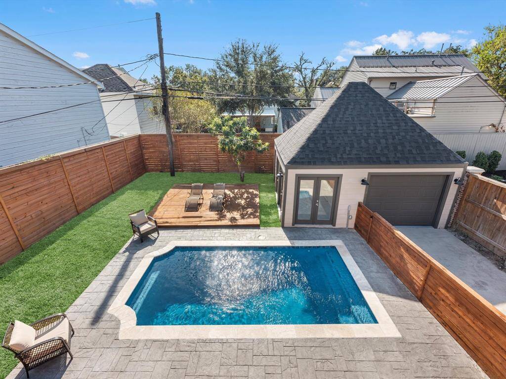 The view from the upstairs balcony overlooks a beautifully designed backyard featuring a sparkling pool, a spacious deck, lush green lawn, and a detached garage with modern finishes.