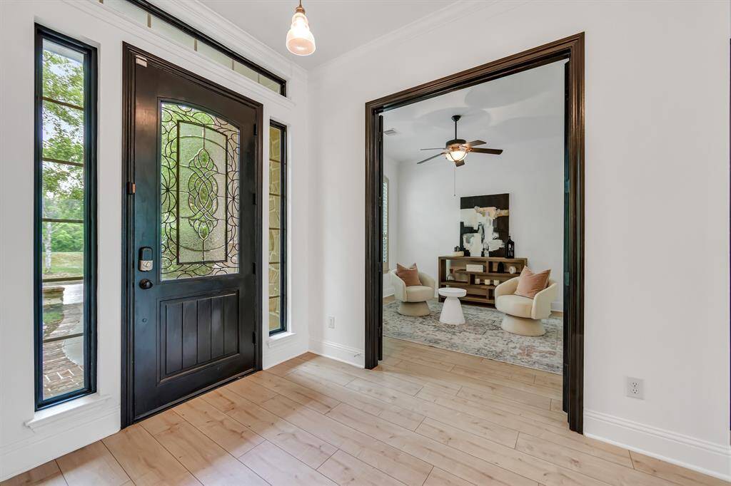 The entrance features a sturdy door with glass panels, providing both strength and a touch of elegance, complemented by light wood tile flooring that extends throughout the space, creating a bright and inviting atmosphere.