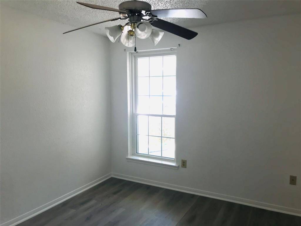 This bright second bedroom has a large window and a ceiling fan. It features light walls and wood-style flooring, with a closet.