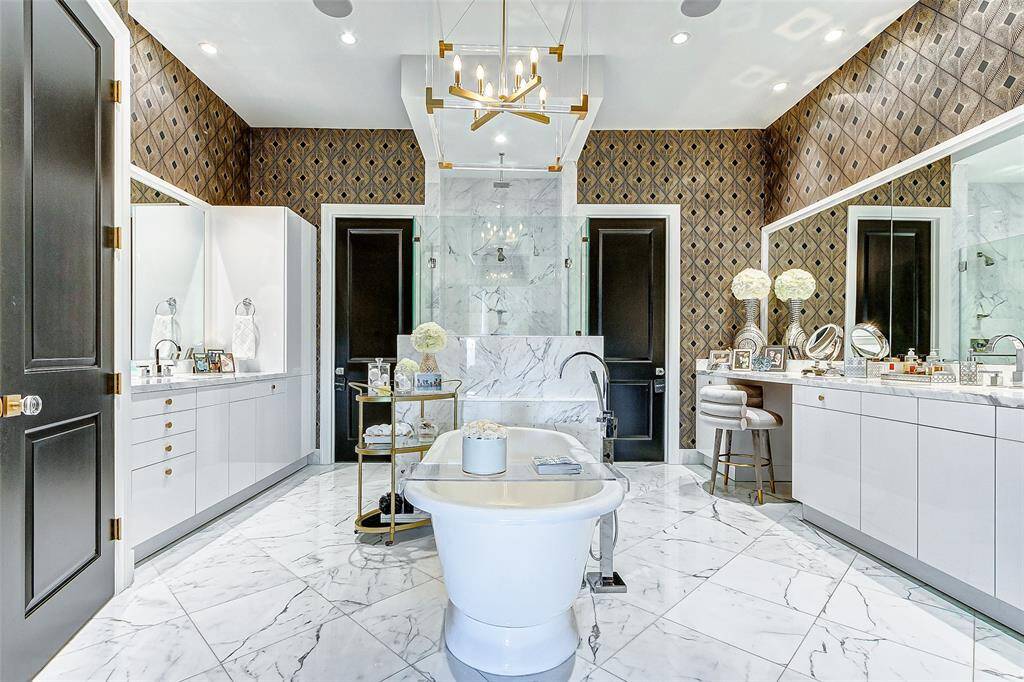 Through a set of double doors, the opulent primary bath features spacious dual vanities with a relaxing central freestanding soaking tub and spacious glass enclosed shower. Beyond the Primary Bath are two enormous walk in closets through the two doors.