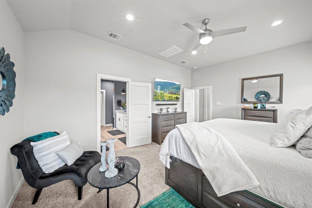 A fresh perspective of the primary suite shows off its peaceful palette, sleek furnishings, and dreamy flow into the en-suite bath.