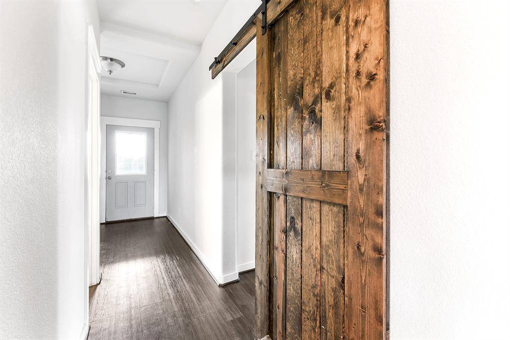 A stylish barn door slides open, providing access to the fourth bedroom, utility room, and the two-car garage, adding both charm and functionality to the space.