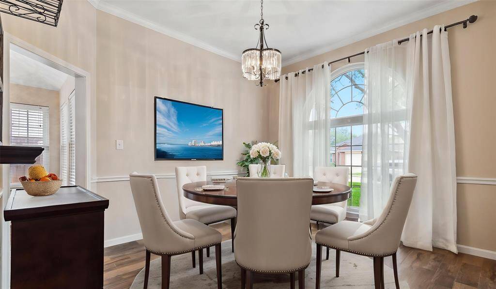 The elegant dining room features a classic chair rail, a large window that fills the space with natural light, a beautiful chandelier serves as the centerpiece, enhancing the space with a touch of sophistication.