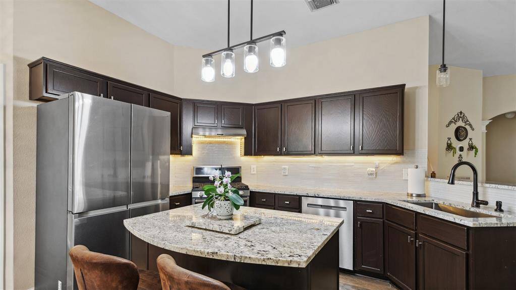 The kitchen seamlessly overlooks the family room, creating an open and inviting atmosphere for entertaining and daily living. Featuring stone countertops, a spacious island with a breakfast bar, and elegant pendant lighting.