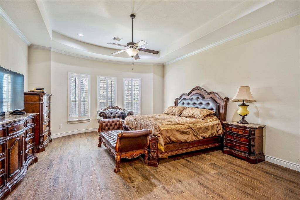 Private primary suite with tray ceiling, wood-look floors, and large windows for serene natural light.