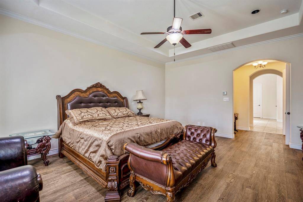 Spacious primary bedroom with ceiling fan and arched hallway entry to spa-inspired bath and closets.