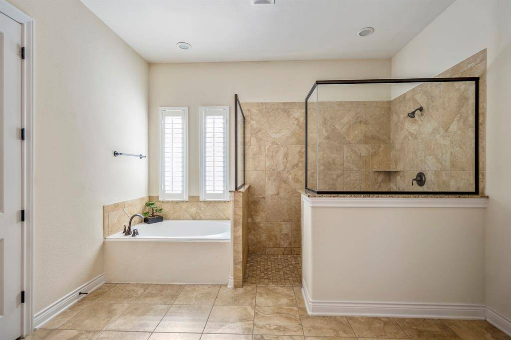 Serene primary bath retreat with a deep soaking tub, frameless glass shower, and natural light from plantation-shuttered windows.