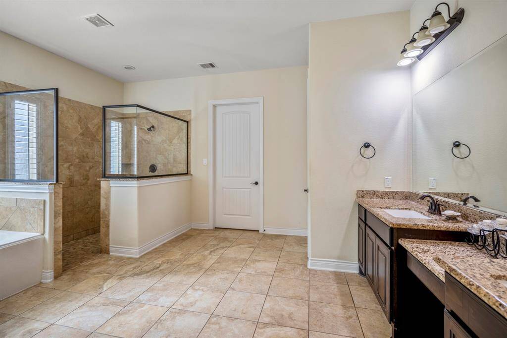 Expansive primary bathroom with dual granite vanities, natural stone tile flooring, and a separate walk-in shower.