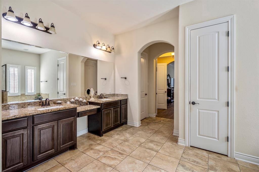 Elegant bathroom vanity with granite countertops, dedicated makeup station, and arched doorway leading to the bedroom suite.