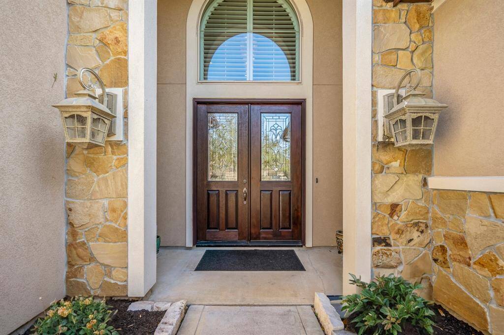 Elegant front entry of this luxury Dunn & Stone home in Lakes of Cypress Forest, Spring, TX. Featuring a grand arched transom window, custom wood double doors with decorative glass panels, and stone-accented exterior.