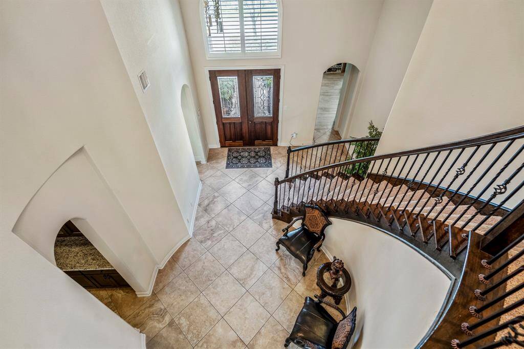 Make a lasting first impression with this dramatic two-story foyer featuring soaring ceilings, a sweeping curved staircase with wrought iron balusters, and rich tile flooring. The double front doors with intricate glass inlays welcome guests with timeless elegance.