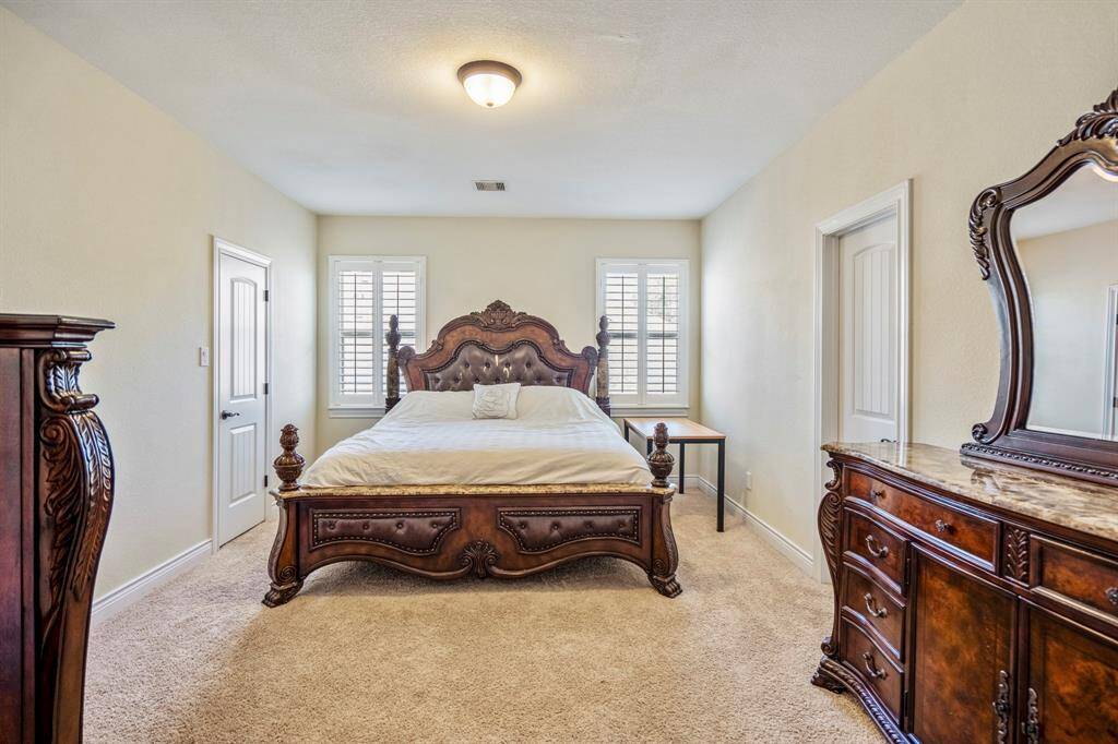 Another generously sized upstairs bedroom boasts warm neutral tones, large windows fill the space with light, enhanced by crisp white plantation shutters.