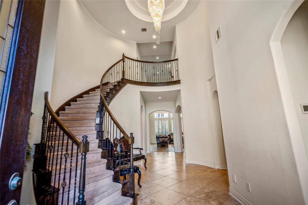 Grand foyer of a luxury home in Lakes of Cypress Forest, Spring, TX, featuring a dramatic curved staircase with wrought iron railing, soaring ceilings, and a statement crystal chandelier.