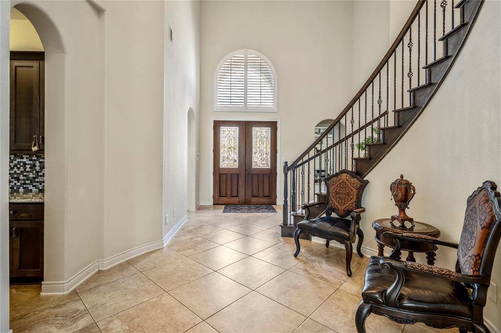Foyer of a luxury home in Spring, TX, featuring elegant double wood entry doors with decorative glass, arched transom window, curved staircase, and tile flooring in a gated community.