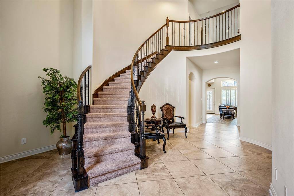 Interior view of a luxury home in Lakes of Cypress Forest showcasing a grand curved staircase with iron spindles, open hallway, and natural light leading into the main living area.