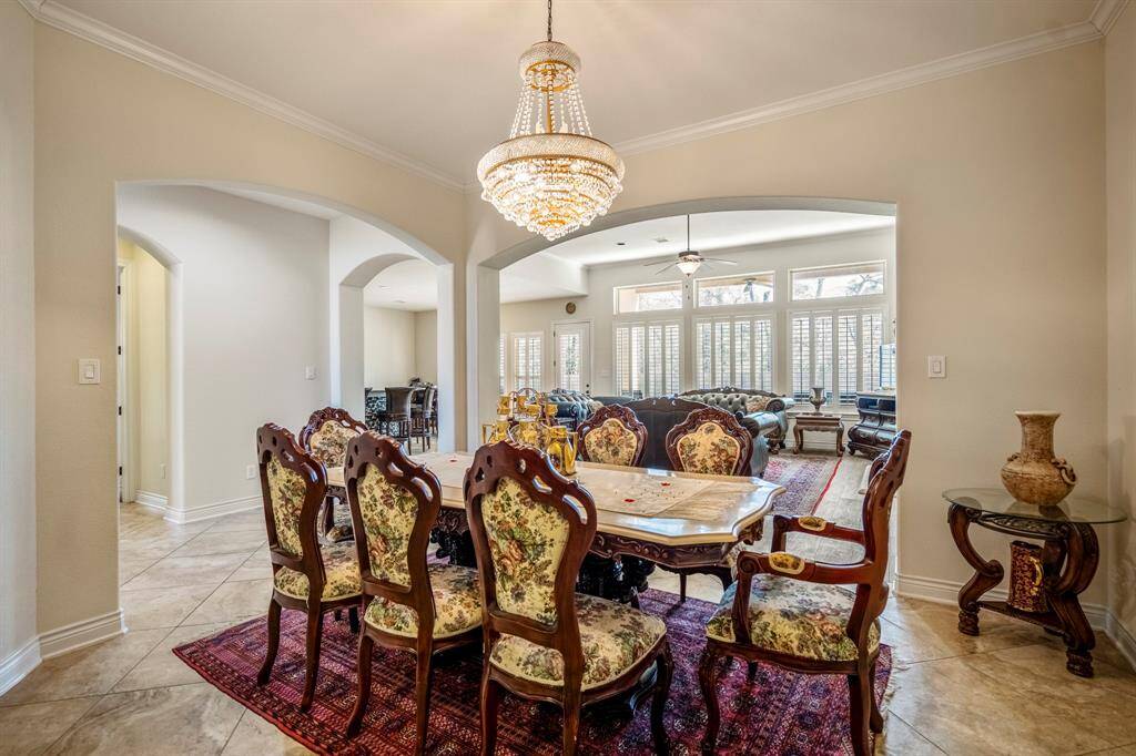 Elegant formal dining room in a luxury Spring, TX home featuring custom furniture, a crystal chandelier, arched entryways, and an open view into the spacious living room with tall windows and natural light.