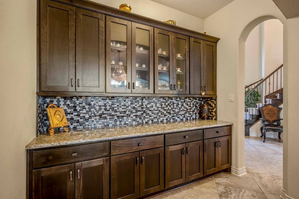 Built-in butler’s pantry with dark wood cabinetry, glass-front upper cabinets, granite countertops, and mosaic tile backsplash.