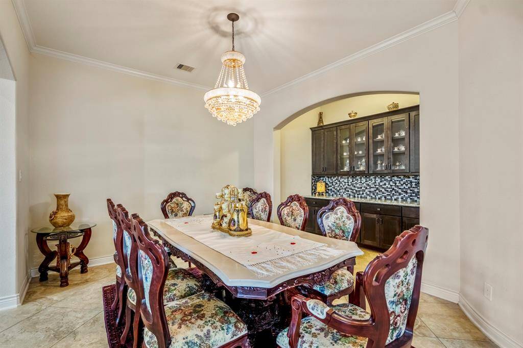 Formal dining room with arched access to a butler’s pantry in a luxury home in Spring, TX. Highlights include neutral wall tones, tray ceiling with chandelier, and tiled floors.