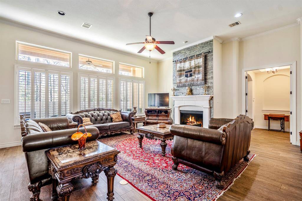 Spacious living area featuring a stone-accented fireplace, elegant crown molding, and tall custom shutter windows that offer natural light and privacy.