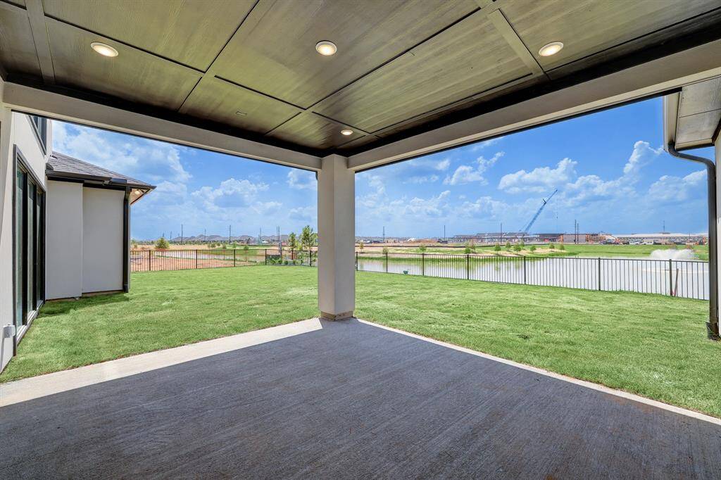This photo showcases a spacious, covered patio with recessed lighting, overlooking a well-maintained lawn and a serene waterfront view, perfect for outdoor relaxation and entertainment.