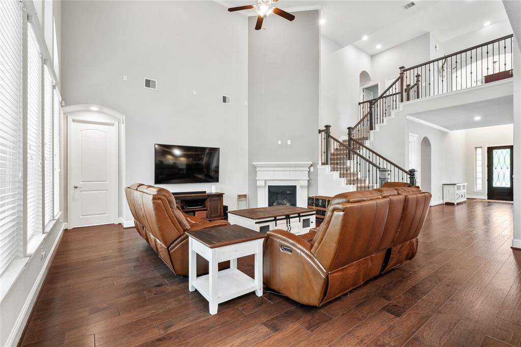 Spacious, elegant living room with high ceilings, hardwood floors, and abundant natural light. Features a cozy fireplace, modern staircase, and open layout, perfect for relaxing or entertaining.
