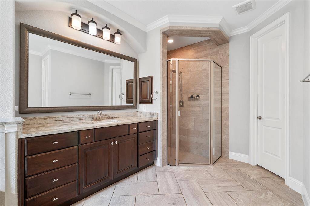 This bathroom features a spacious design with a large vanity, granite countertop, and ample storage. It has a modern glass-enclosed shower, elegant tile flooring, and a soft, neutral color palette.
