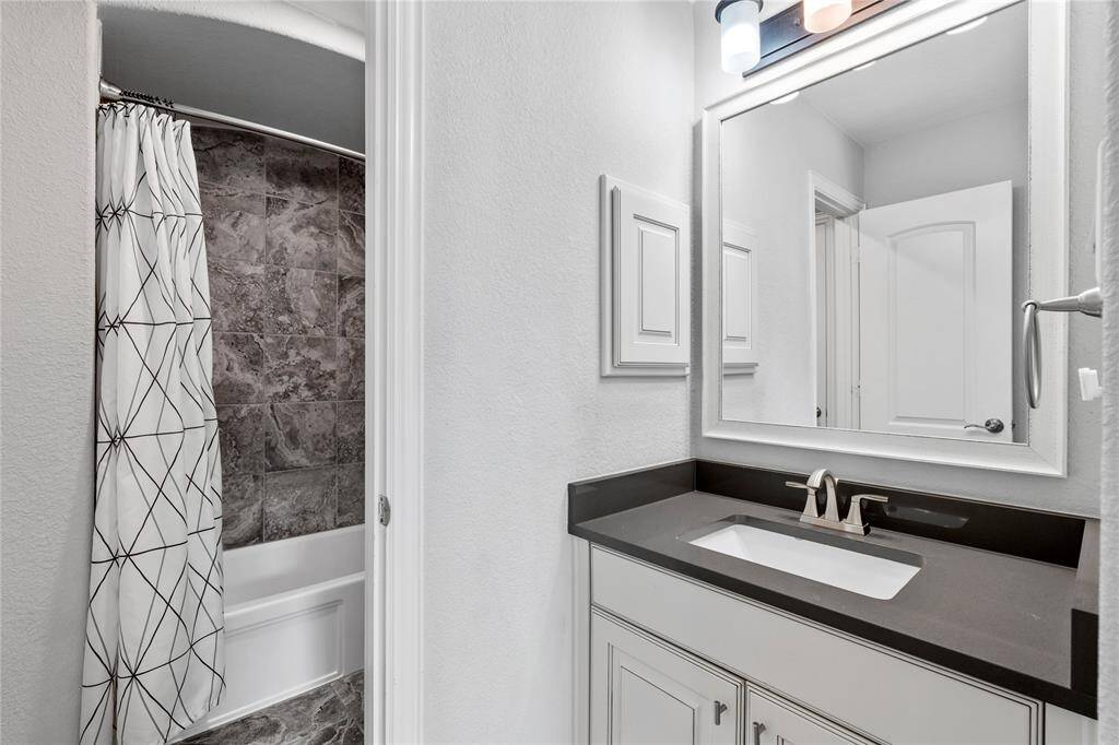 This bathroom features a modern design with a sleek dark countertop, integrated sink, and stylish fixtures. The shower area has elegant stone tile and a patterned curtain, providing a clean and contemporary look.