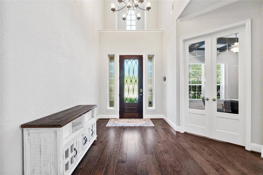 This entryway features high ceilings, a stylish chandelier, and a decorative glass front door flanked by sidelights. It has rich wood flooring, creating an inviting and elegant first impression.