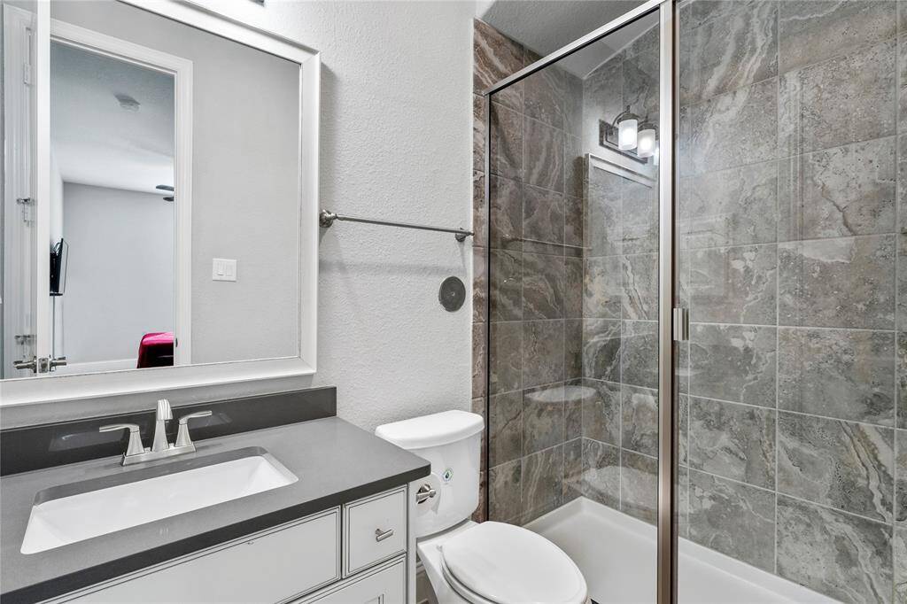 This modern bathroom features a sleek design with a glass-enclosed shower, elegant gray tile, a large mirror, and a stylish vanity with ample storage.