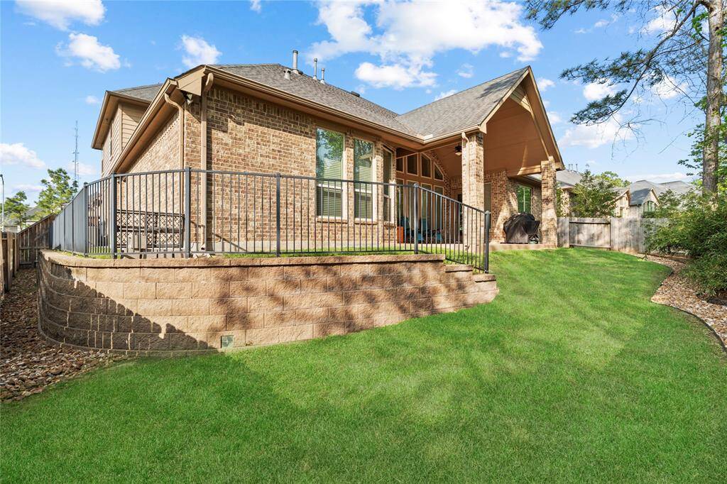 Elevated backyard has a grassy lawn, a stone retaining wall, and a covered patio. The space is perfect for outdoor relaxation and entertaining.
