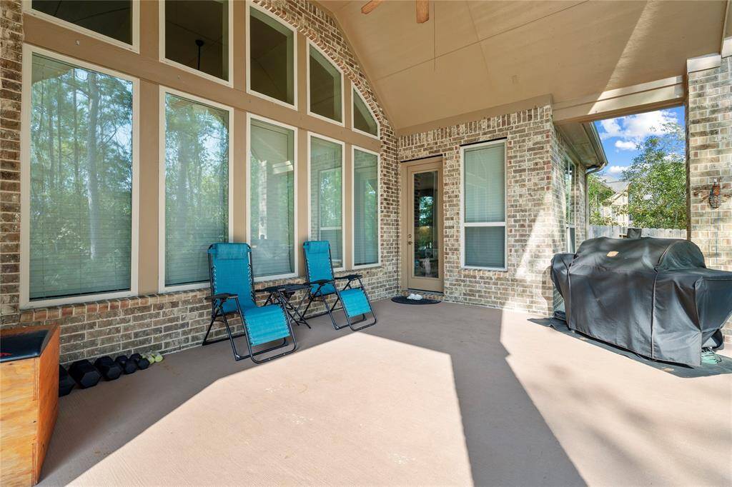 This spacious covered patio features large windows, allowing natural light to fill the area. It includes comfortable seating and space for a grill, perfect for outdoor entertaining. The brick exterior adds a charming touch, while the surrounding trees offer a sense of privacy and tranquility.