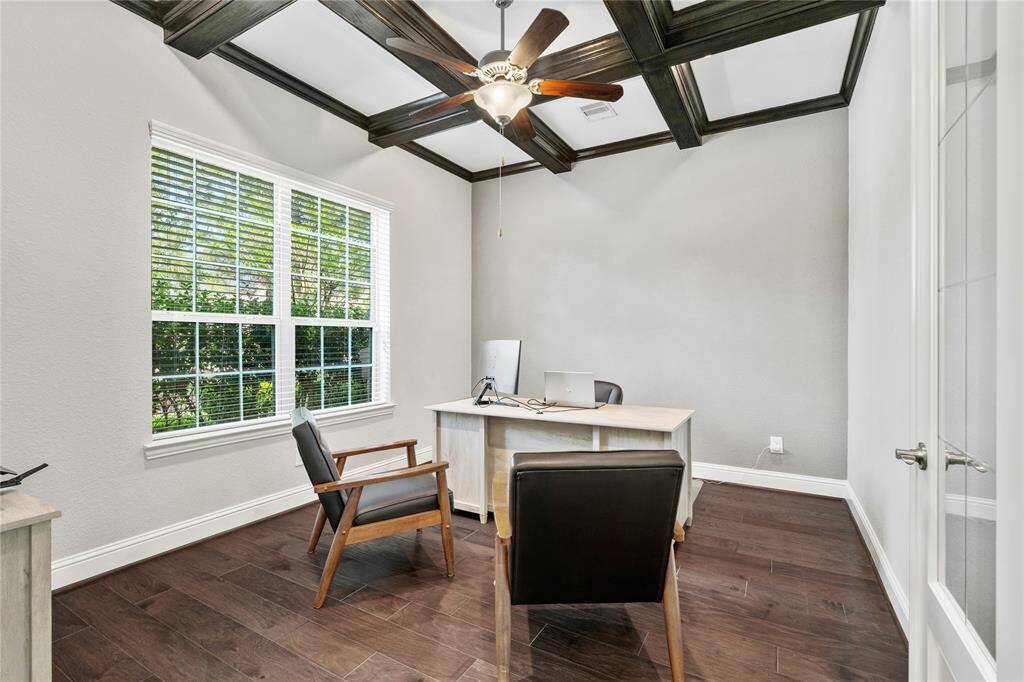 Bright and inviting home office with large window, elegant coffered ceiling, ceiling fan, and hardwood floors, perfect for productivity.
